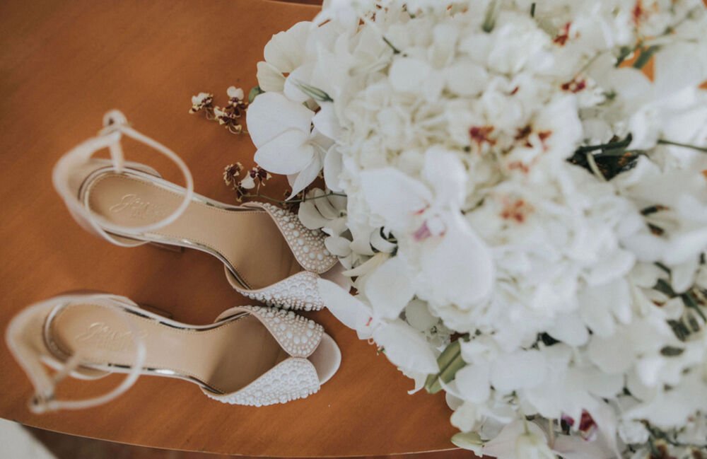 Zapatos de novia junto a un ramo de orquídeas blancas